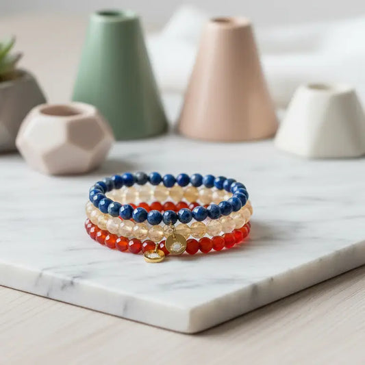 Citrine, Carnelian, and Lapis Lazuli faceted beaded bracelets with gold charms on a marble support and geometric shapes in the blurred background