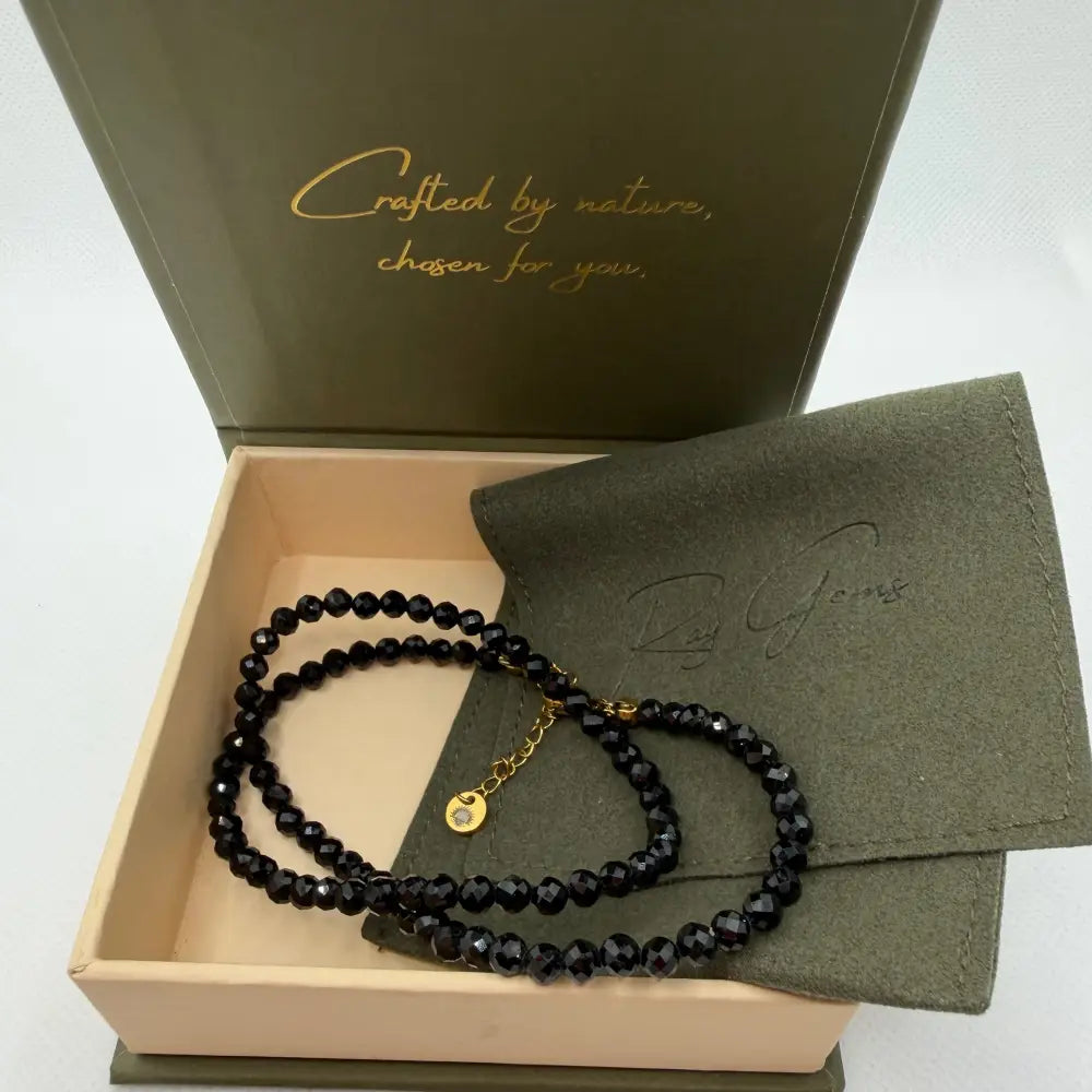 Obsidian Faceted Necklace with gold charm on an olive green pouch in a cream and olive green branded box and light background
