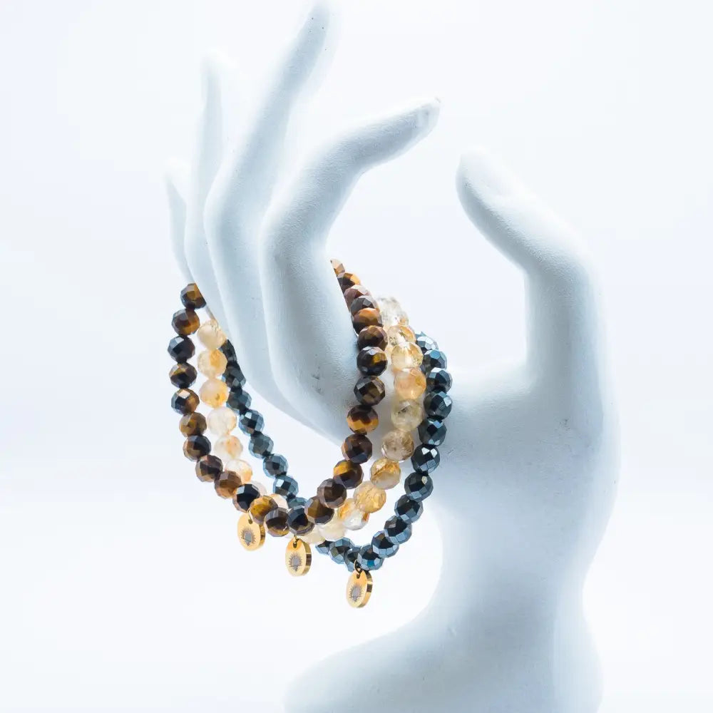 Set of Tiger Eye, Hematite, and Citrine faceted beaded bracelets with gold charms on a white mannequin hand against a white background