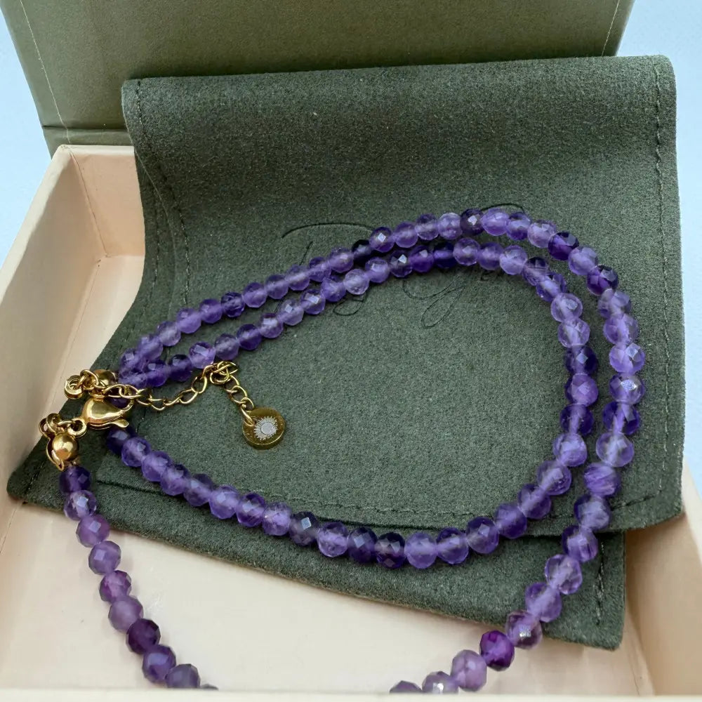 Amethyst Faceted Round Necklace with gold charm on an olive green pouch in a cream and olive green box