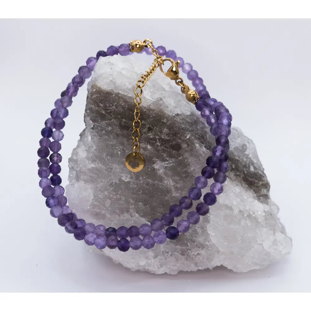 Amethyst Faceted Round Necklace with gold charm on a white and grey stone and a light background