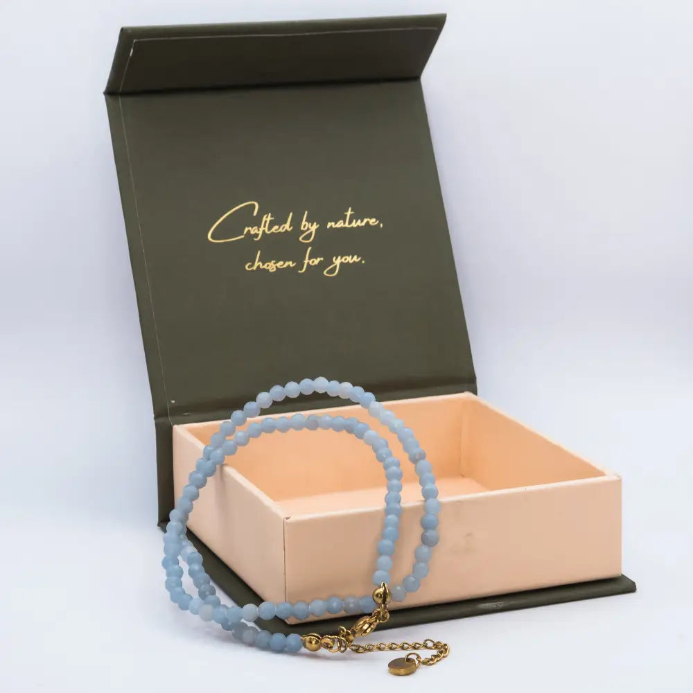 Angelite Faceted Necklace with gold charm on a cream and olive green branded box with light grey background