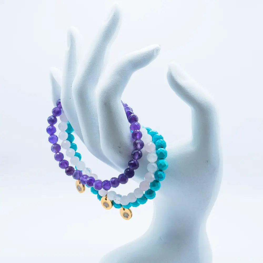 Rose Quartz, Amethyst, and Turquoise faceted beaded bracelet with gold charms on a hand-like shape stand and white background