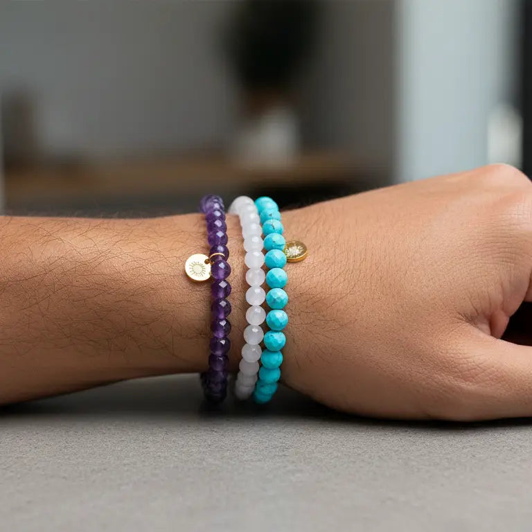 Rose Quartz, Amethyst, and Turquoise faceted beaded bracelets with gold charms on a wrist and blurred indoor background