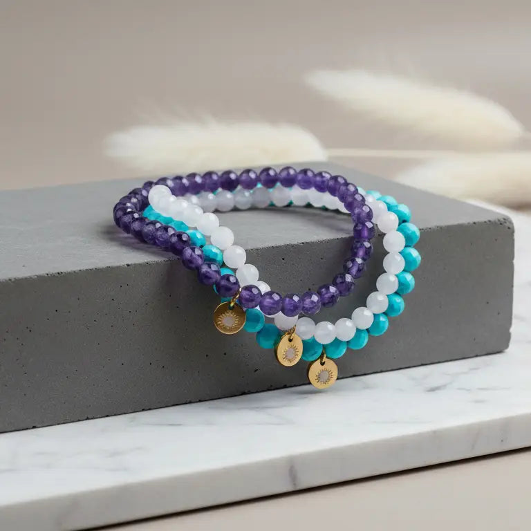 Rose Quartz, Amethyst, and Turquoise faceted beaded bracelets with gold charm on a stone and marble stand and light grey background