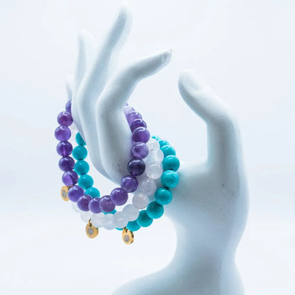 Rose Quartz, Amethyst, and Turquoise beaded bracelets with gold charms on a mannequin hand and white background