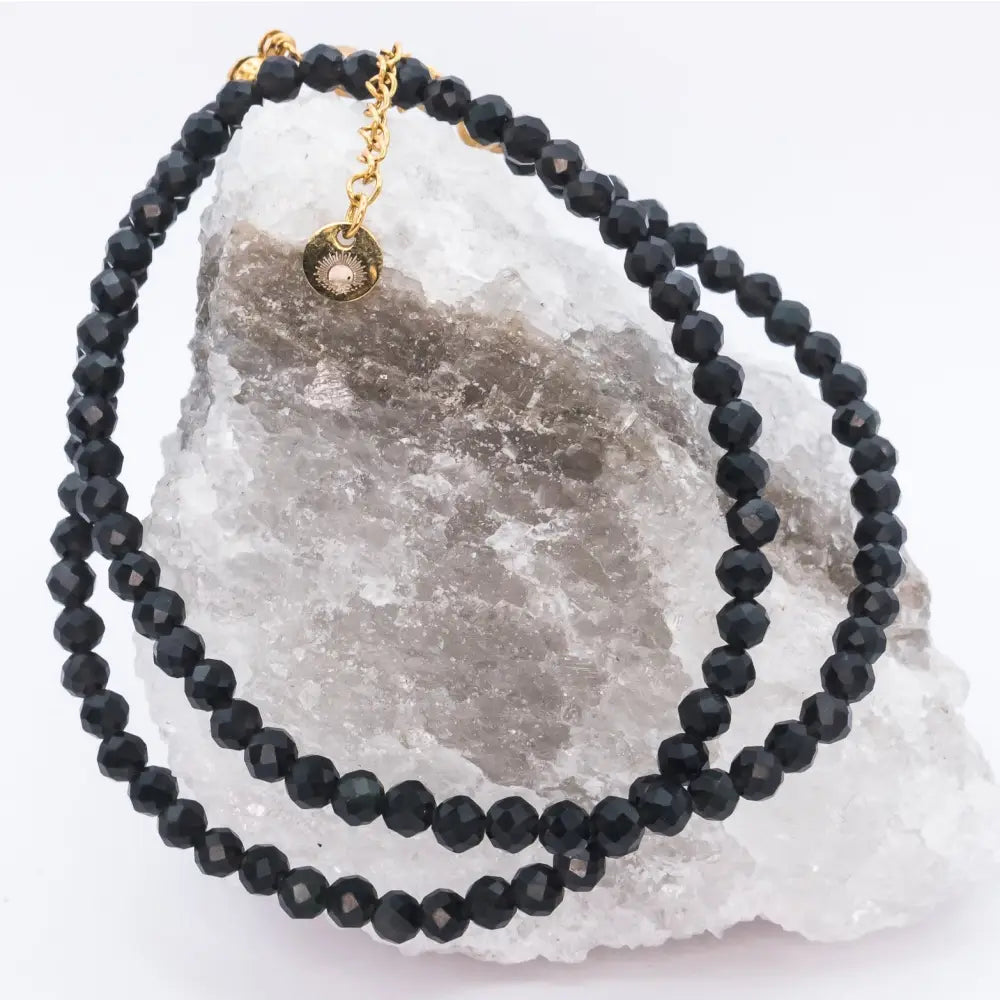 Black Tourmaline Faceted Necklace with gold charm on a white and grey stone with light background