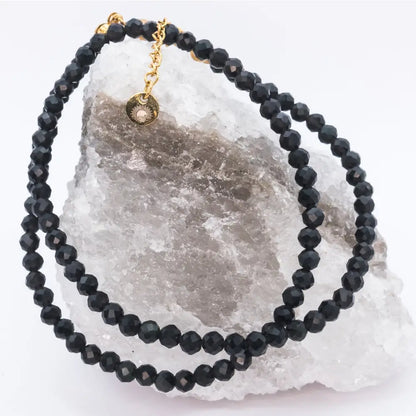Black Tourmaline Faceted Necklace with gold charm on a white and grey stone with light background