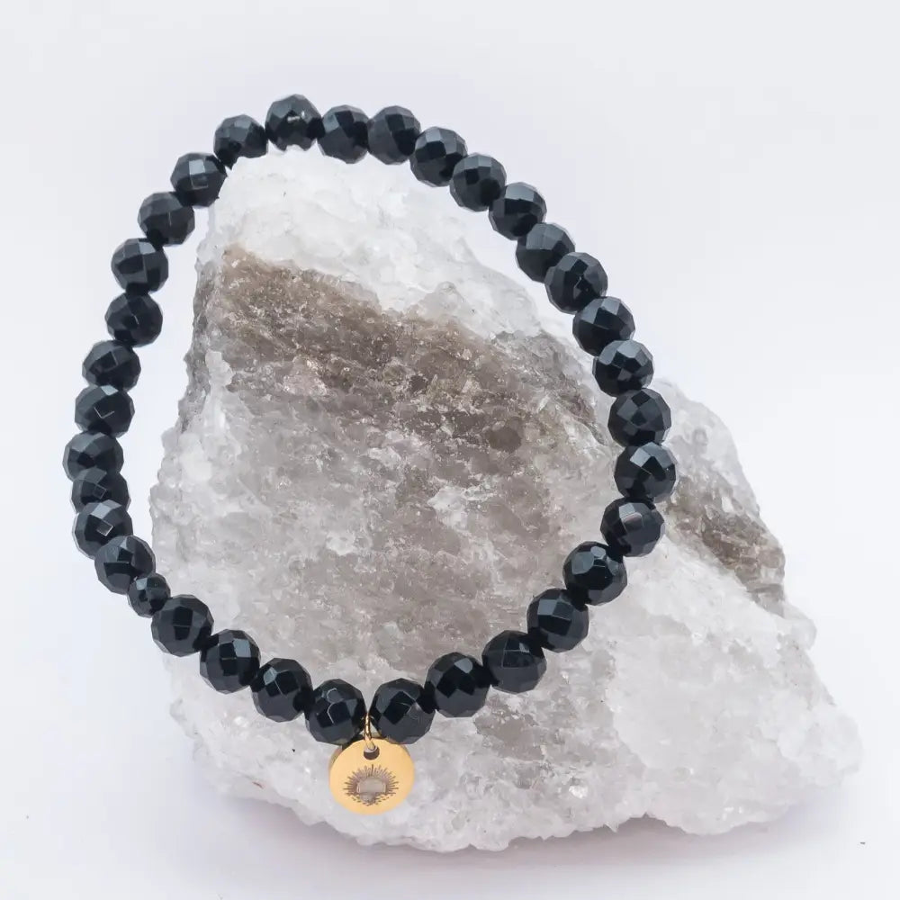 Black Tourmaline Faceted Bracelet with gold charm on a white and grey stone and light background