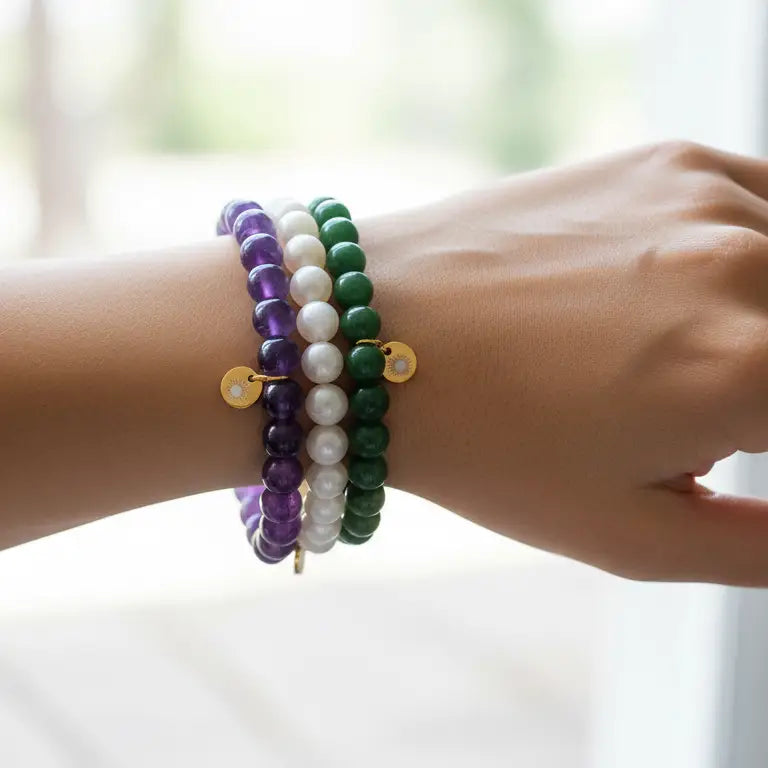 Amethyst, Moonstone, and Nephrite Jade beaded bracelets with gold charms on a wrist and blurred background