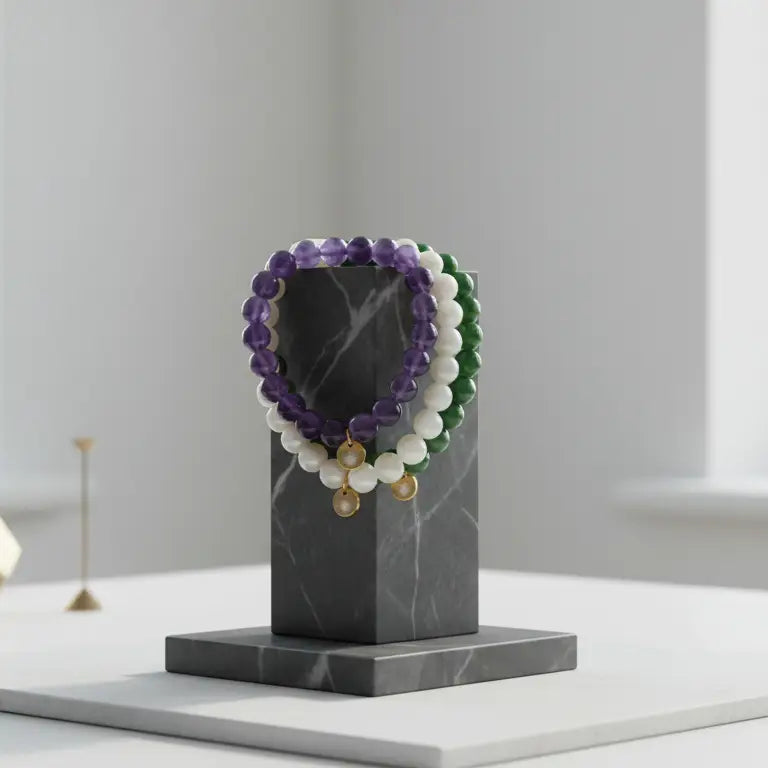 Amethyst, Moonstone, and Nephrite Jade beaded bracelets with gold charms on a geometric marble stand and blurred neutral background