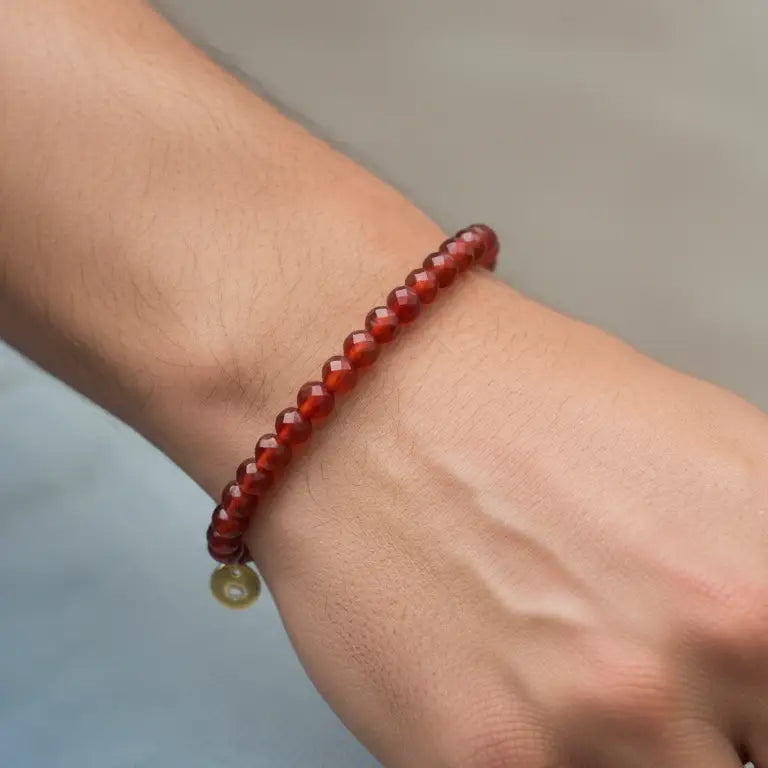 Carnelian Faceted Bracelet with gold charm on a wrist with a light grey background