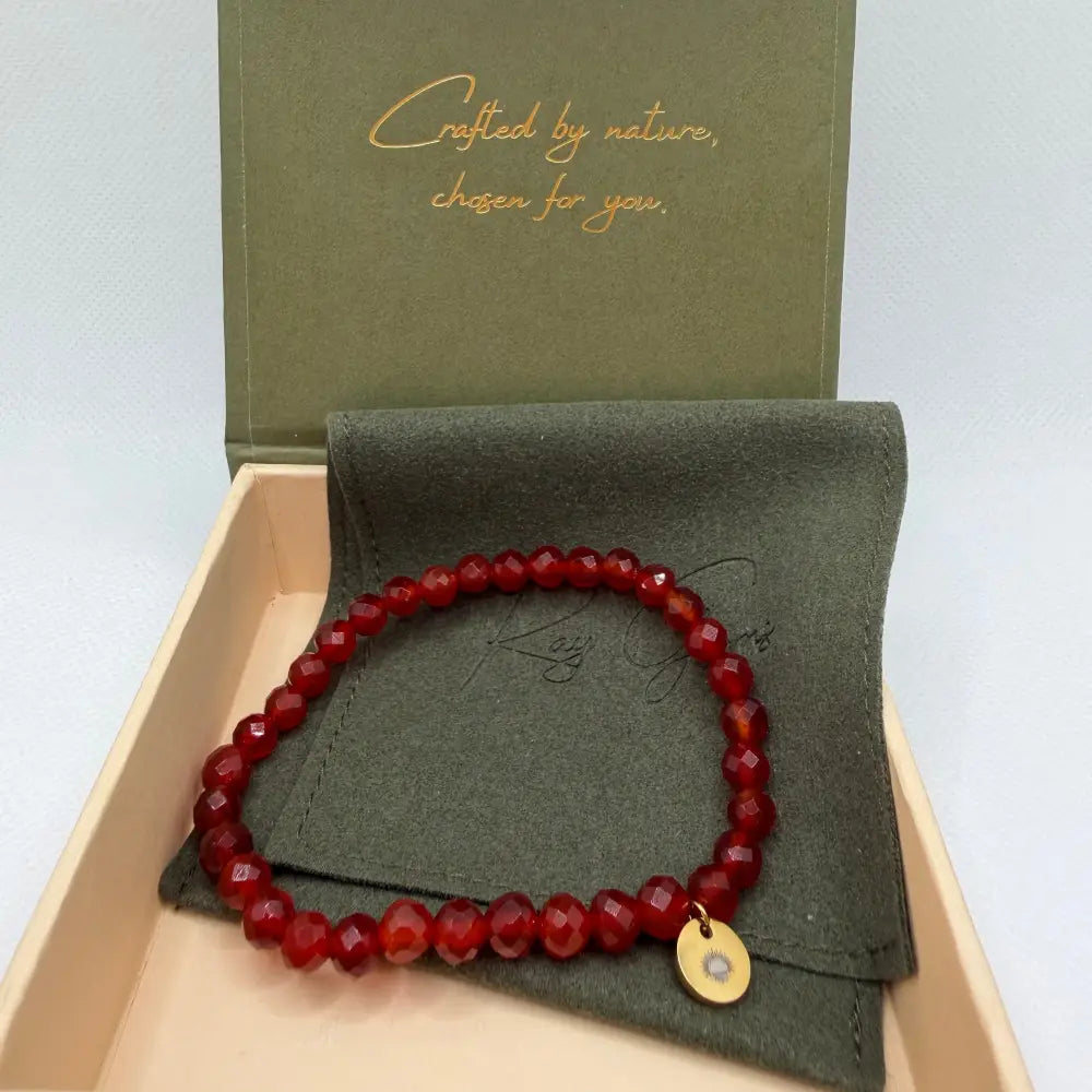 Carnelian Faceted Bracelet with gold charm on an olive green pouch in a cream and olive green branded box 