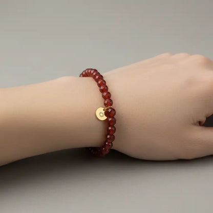 Carnelian Faceted Bracelet with gold charm on a wrist and a neutral background