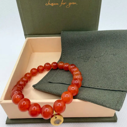 Carnelian Beaded Bracelet with gold charm on an olive green pouch in a cream and olive green branded box