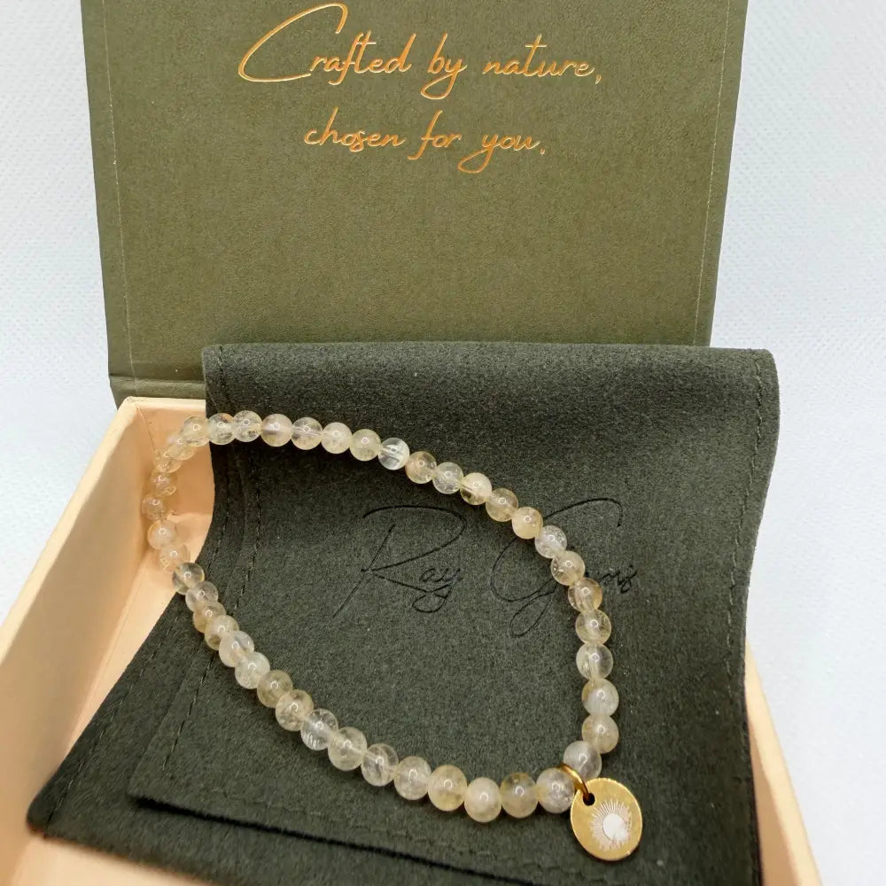 Citrine Beaded Bracelet with gold charm on an olive green pouch in a cream and olive green branded box