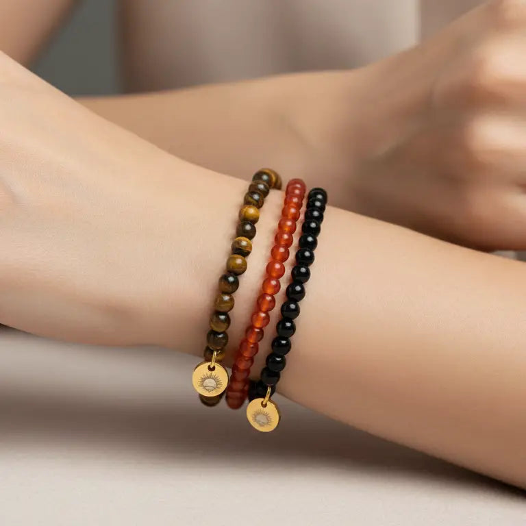 Tiger Eye, Carnelian, and Obsidian beaded bracelets with gold charms on a wrist with neutral background