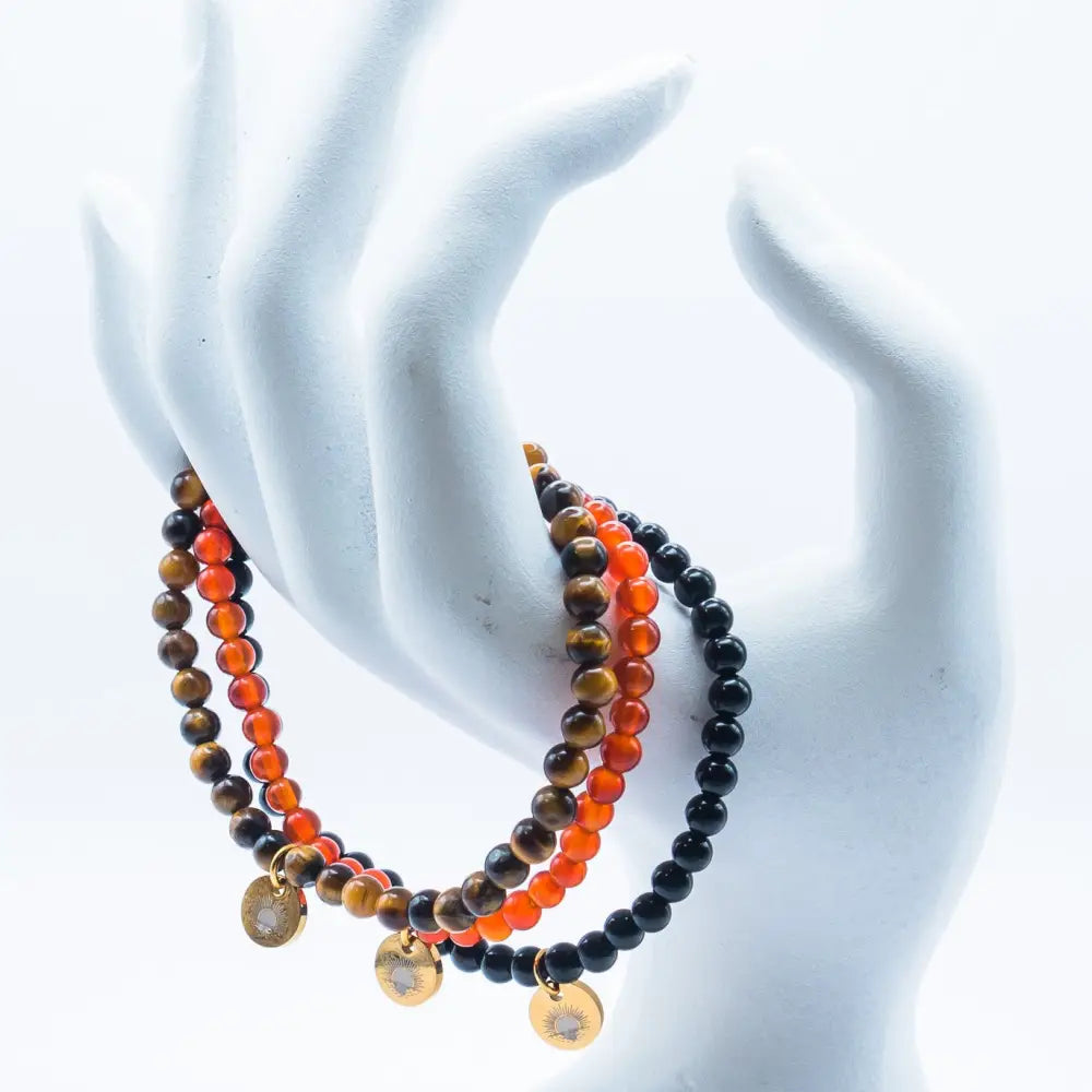 Tiger Eye, Carnelian, and Obsidian beaded bracelets with gold charms on a hand-like stand and white background