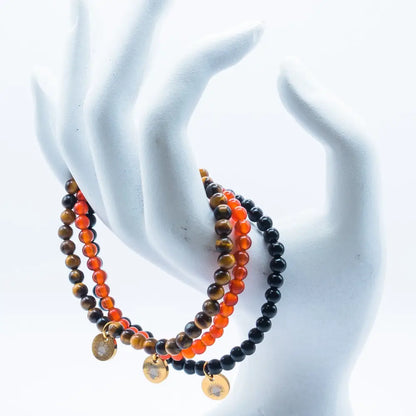 Tiger Eye, Carnelian, and Obsidian beaded bracelets with gold charms on a hand-like stand and white background