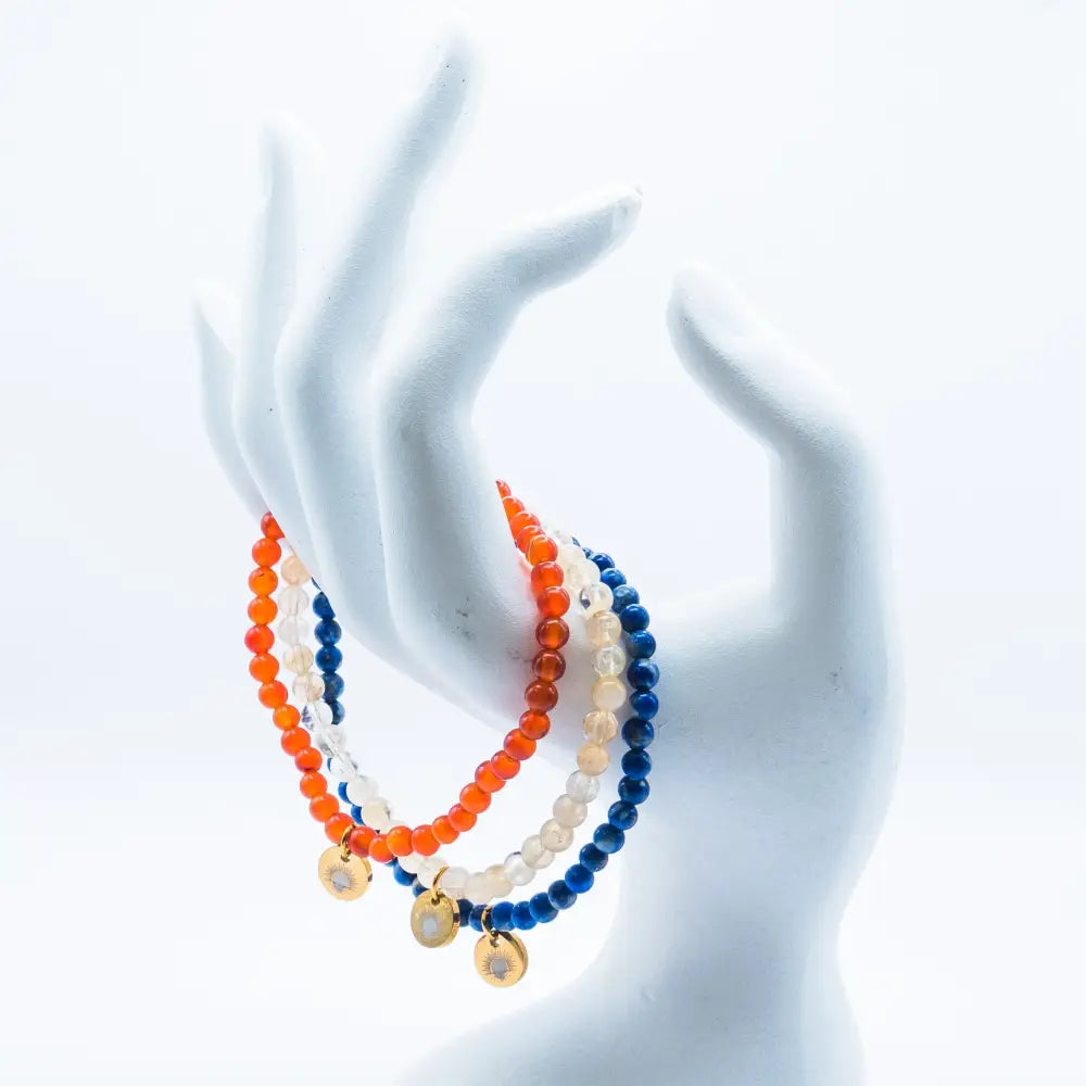 Citrine, Carnelian, and Lapis Lazuli beaded bracelets with gold charms on a mannequin hand and white background