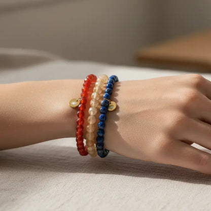Citrine, Carnelian, and Lapis Lazuli faceted beaded bracelets with gold charms on a wrist and neutral blurred indoor background