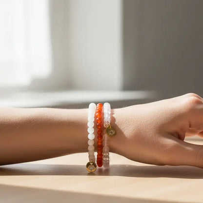 Moonstone, Carnelian, and Rose Quartz beaded bracelets with gold charms on a wrist and blurred neutral background