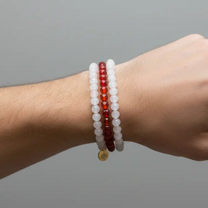 Moonstone, Carnelian, and Rose Quartz faceted beaded bracelets with gold charm on a wrist with light grey background