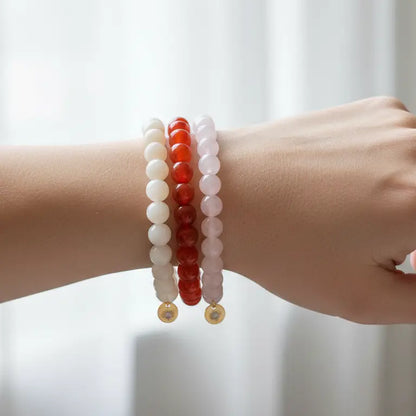 A hand with Moonstone, Carnelian, and Rose Quartz beaded bracelets wth gold charms and light blurred background