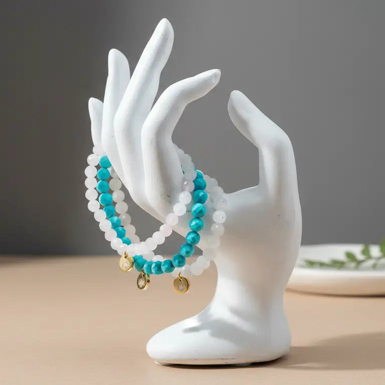 Moonstone, Turquoise, and Rose Quartz faceted beaded bracelets on a neutral surface with a plate and plant and light grey blurred background