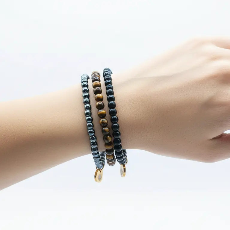 Tiger Eye, Hematite, and Obsidian beaded bracelet with gold charms on a wrist and light grey background