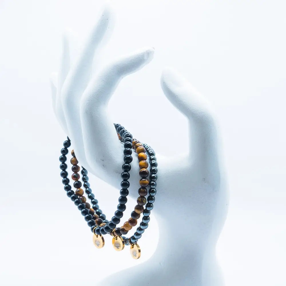 Tiger Eye, Hematite, and Obsidian beaded bracelets with gold charms on a hand-like stand and white background