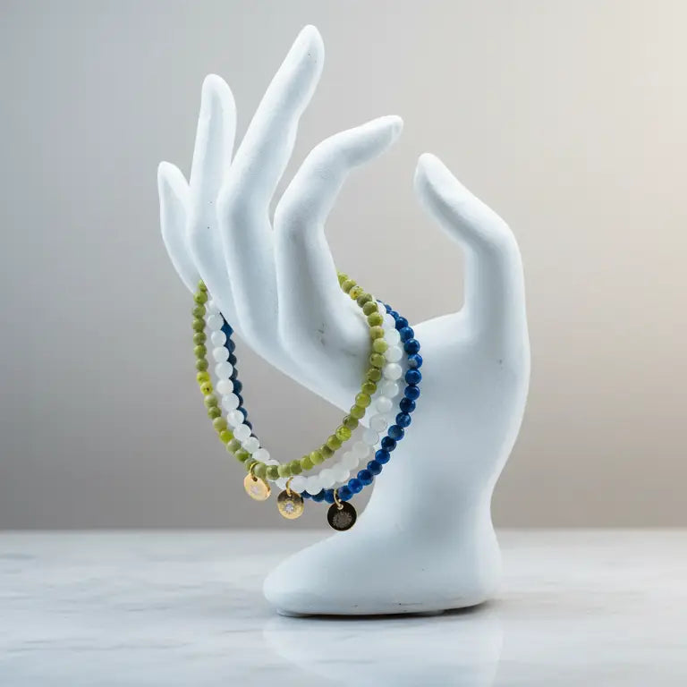 Peridot, Moonstone, and Lapis Lazuli beaded bracelets with gold charms on a hand-like stand with neutral background