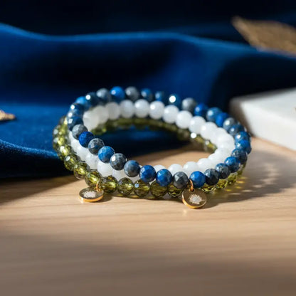 Peridot, Moonstone, and Lapis Lazuli faceted beaded bracelet with gold charms against a dark blue fabric and blurred background