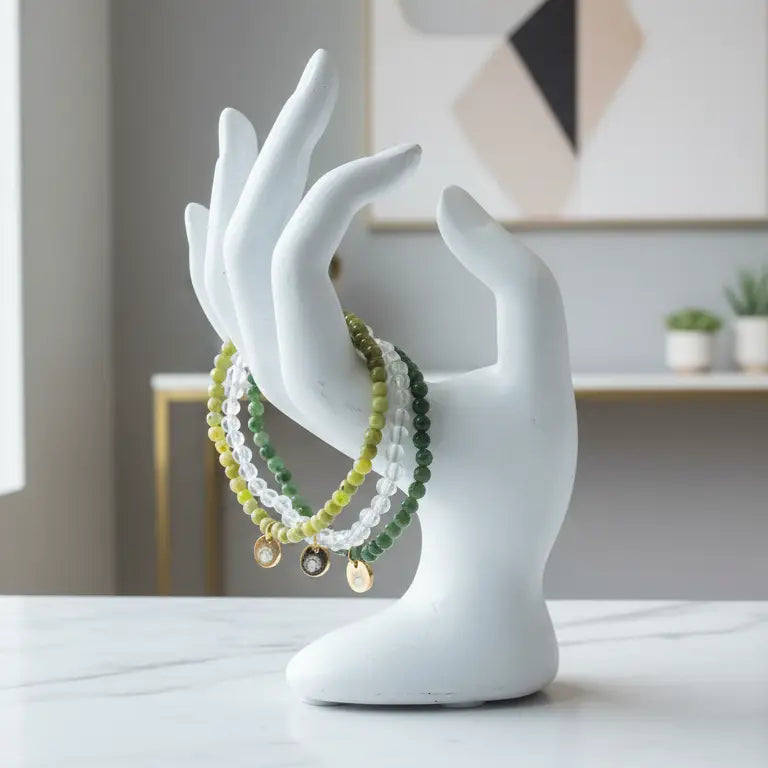 Rose Quartz, Peridot, and Nephrite Jade beaded bracelets with gold charm on a white sculpture of hands against an indoor background