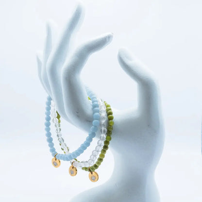A set of Rose Quartz, Angelite, and Peridot beaded bracelets with gold charms on a mannequin hand with white background