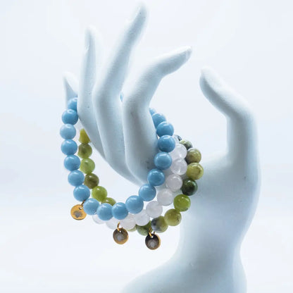 Rose Quartz, Angelite, and Peridot beaded bracelets with gold charms on a mannequin hand with white background