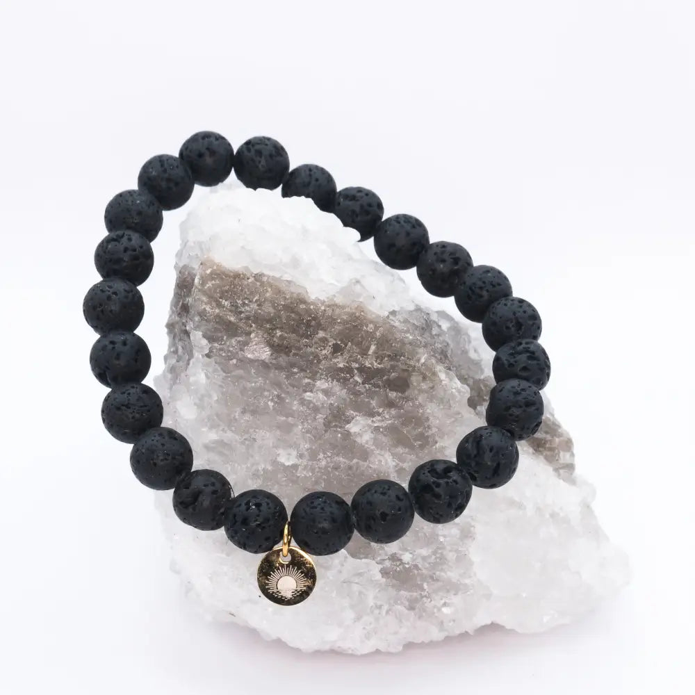 Lava Stone Beaded Bracelet with gold charm on a white and grey stone with light background