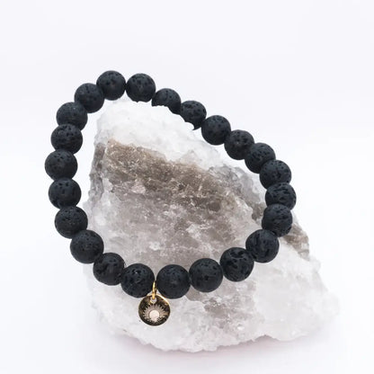 Lava Stone Beaded Bracelet with gold charm on a white and grey stone with light background