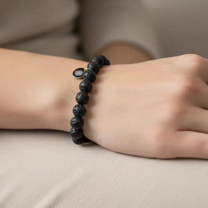 Lava Stone Beaded Bracelet with gold charm on a wrist and neutral blurred background