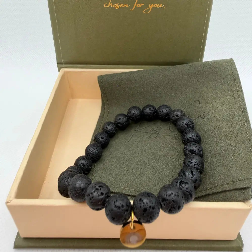 Lava Stone Beaded Bracelet with gold charm on an olive green pouch in a cream and olive green branded box