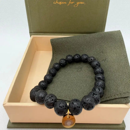 Lava Stone Beaded Bracelet with gold charm on an olive green pouch in a cream and olive green branded box