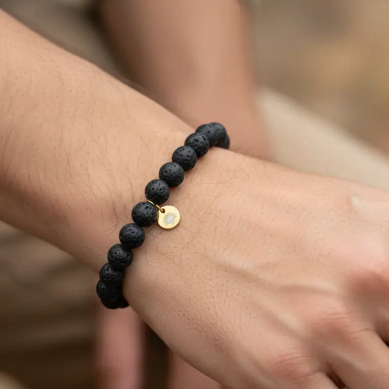 Lava Stone Beaded Bracelet with gold charm on a wrist and blurred background