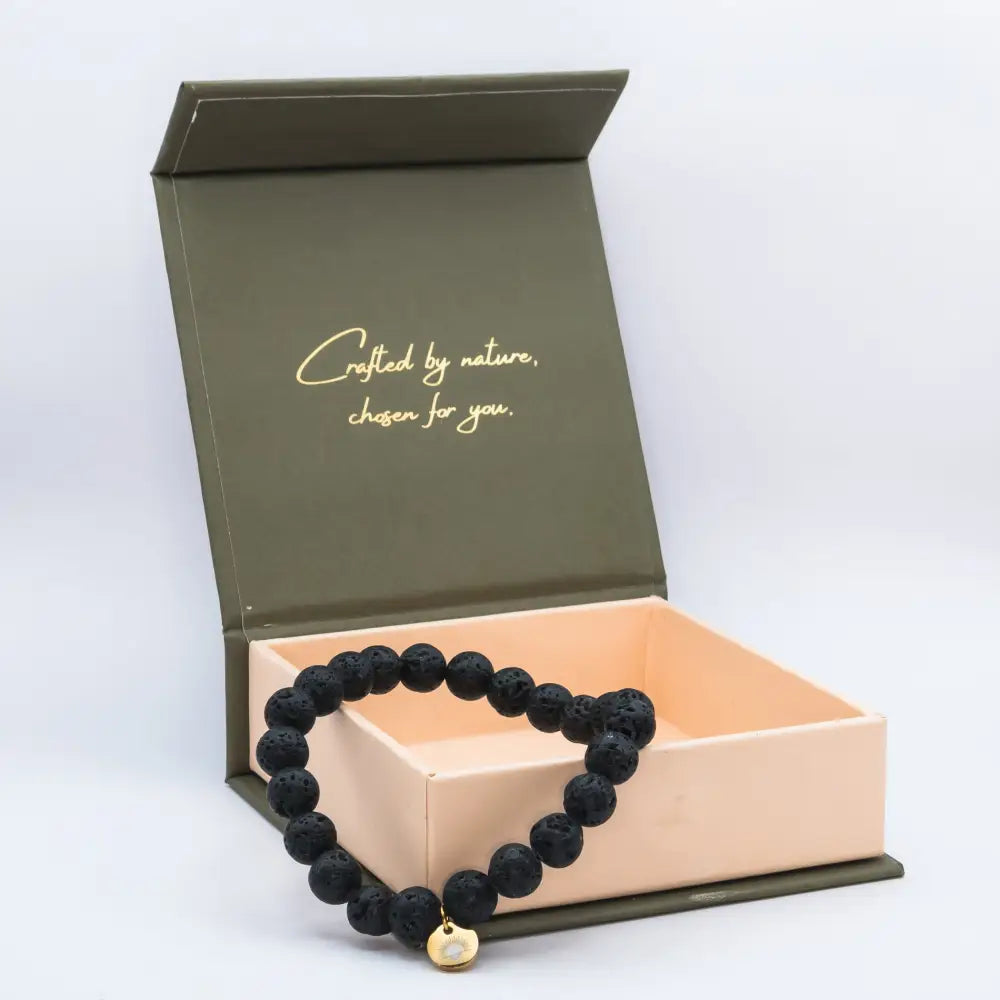 Lava Stone Beaded Bracelet with gold charm on a cream and olive green branded box and light grey background