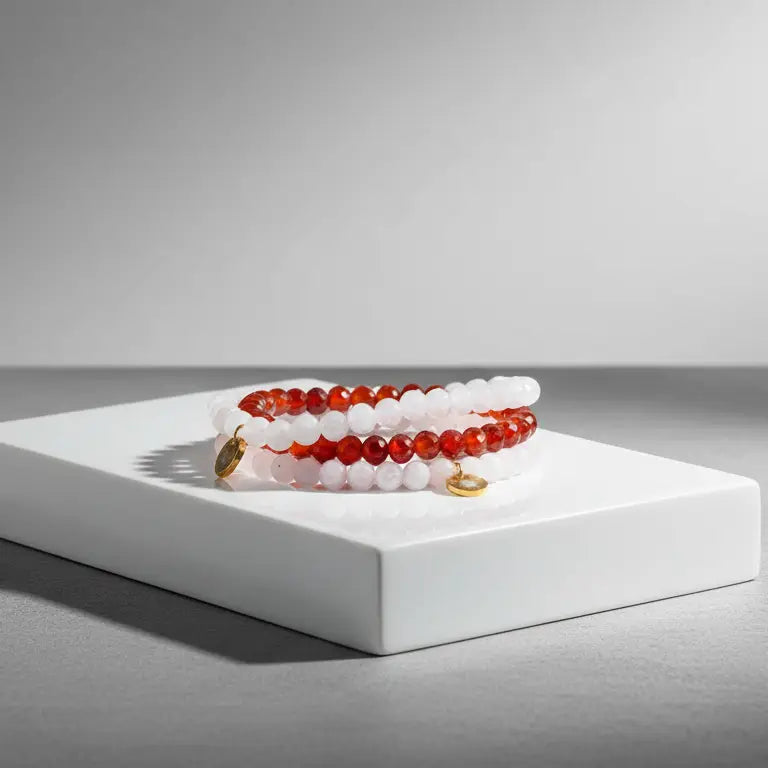 Set of Rose Quartz, Moonstone, and Carnelian beaded bracelets with gold charms on a white platform with a gray background