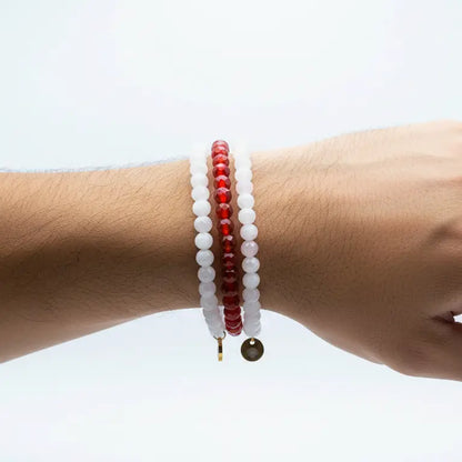 Hand wearing a set of Rose Quartz, Moonstone, and Carnelian beaded bracelet with gold charms on a plain background