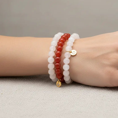 Hand wearing Rose Quartz, Moonstone, and Carnelian beaded bracelets with gold charms on a neutral background
