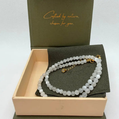 Moonstone Beaded Necklace with gold charm on an olive green pouch in a cream and olive green branded box
