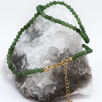 Nephrite Jade Beaded Necklace with gold charm on a white and grey stone and white background