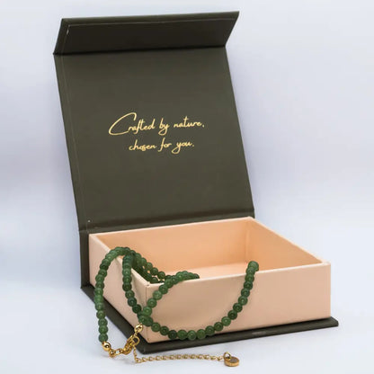 Nephrite Jade Beaded Necklace with gold charm on a cream and olive green box with light grey background