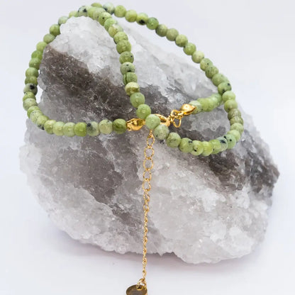 Peridot Beaded Necklace with gold charm on a white and grey stone with a neutral background